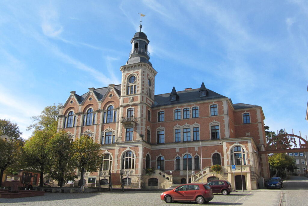 Rathaus aus Backstein mit hohem Turm. Davor liegt ein gepflasterter Platz.