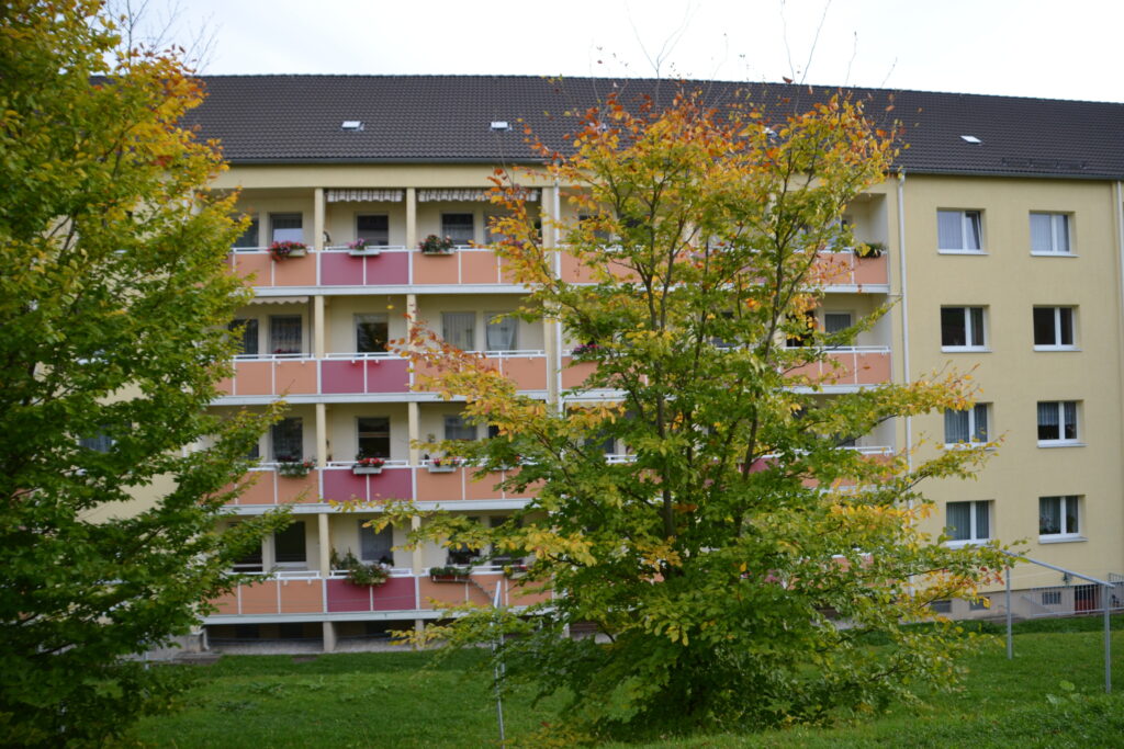 Wohnhaus mit Balkonen, davor Bäume in Herbstfarben.